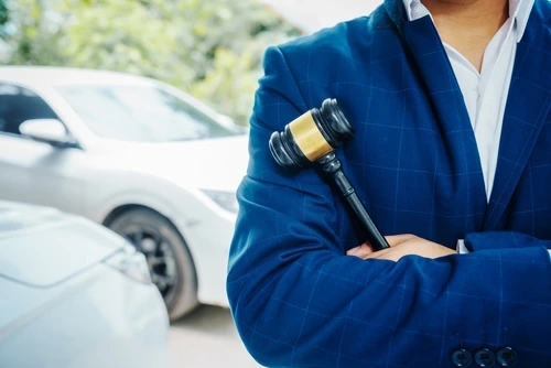 A Houston car accident lawyer stands near a vehicle holding a judgeโs gavel.