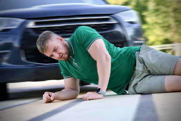 A pedestrian is hit by a car in a crosswalk.
